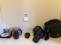 All items laid out on table: camera with attached lens and strap; separate lens; lens hood; carrying pouch; UV filter; software CD; camera bag