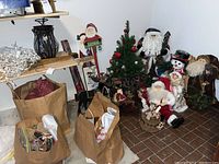 Photo showing Christmas tree, multiple Santa and snowman figurines, reindeer candelabra, signs, and paper bags with decorations on floor