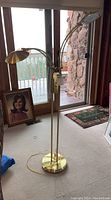 Full view of the gold floor lamp standing on carpet near a window and stone wall.