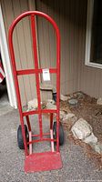 Front view of heavy red metal wheeled dolly showing handle, frame and loading plate.