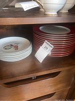 Photo of stacked Crate & Barrel white center plates with red rim and stacked white elf design plates.