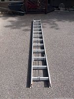 Full length photo of aluminum extension ladder laid flat on asphalt surface, showing overall condition and length.