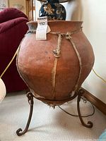 Front view of large pottery planter or vase showing round shape, rope binding, and metal stand with curled feet.