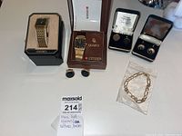 Overview of two gold-tone watches in boxes, two sets of cufflinks and a sealed chain bracelet on table