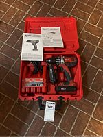 Milwaukee cordless driver drill kit inside open red case including battery, charger, manuals, and accessories.