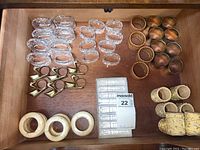 Wooden drawer with multiple types of napkin rings including glass, metal, woven, and decorative rings.