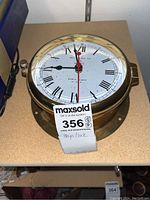 Front view of Bell Clock Co. quartz ship's clock with Roman numerals, brass casing, clock tag and label visible.