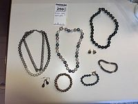 Overview of the jewelry lot showing all necklaces, bracelets and earrings arranged on white surface.
