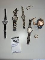 Full view of all jewelry items on flat surface: five wristwatches, metal ring, and pair of gold-colored earrings.