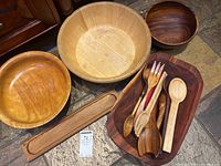 Top view of four wooden bowls and assorted wooden utensils arranged on floor.
