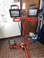 Front view of the Husky dual-head 1000 watt work light mounted on red tripod stand with cords coiled around the tripod.