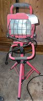 Pink tripod work light with foam handle, protective metal cage on light, and wrapped power cord.