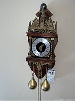 Front view of Zaanse-style vintage Dutch wall clock showing brass figurines and weights, wooden case, and clock face with Roman numerals.