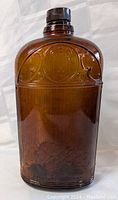 Front and angled view of an antique amber glass whiskey bottle showing embossed ornamental details and overall shape.