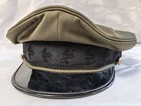 Front side view of Canadian military soldier hat showing olive green top, black embroidered band with maple leaf emblem, shiny black visor, and gold-tone buttons on sides.