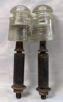 Front view of two clear glass insulators on wood posts showing embossed text on glass.