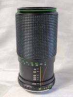 Close-up front view showing textured grip, aperture ring, distance markings and green ring on front element.