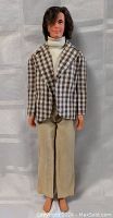 Full body front view of vintage 12-inch Ken doll dressed in plaid jacket, white turtleneck, and beige pants, standing against a plain backdrop.