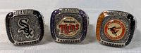 Front view of all three baseball championship rings showing logos for Chicago White Sox, Minnesota Twins, and Baltimore Orioles with 'World Series Champions' text.