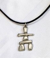 Close-up of the silver-tone Inukshuk pendant showing its geometric stacked stone design on a white background.