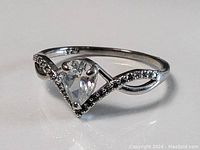 Close-up image of sterling silver ring with pear-shaped clear stone and decorative beaded accents on band, stamped 925 inside.