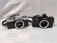 Two Minolta SLR film cameras, one silver XG1 and one black XE7, both without lenses.