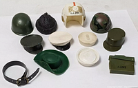 Various vintage toy soldier helmets, hats, caps, and accessories arranged on white background.