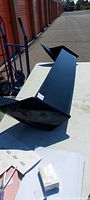 Black Bomex rear wing/spoiler placed on a white table outside with storage units in the background.