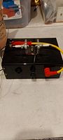 Photo of black spark plug tester box with attached red and yellow test cables and analog gauge.