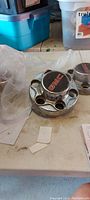 Four chrome GMC wheel center caps with red GMC logo on a table with plastic wrapping and some paper tags