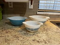 Three Pyrex bowls on countertop, two with blue decorative band pattern and one solid blue.