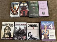 Top-down image showing 7 DVDs and 4 VHS tapes arranged on carpet. Titles visible include The Great Indian Wars, Canada at War, One Flew Over the Cuckoo's Nest, Janis Saffell Workout, Heavy Metal, Akira, Fearless, and Delivery Academy martial arts.