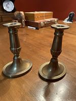 Pair of antique solid brass English candle holders standing on wooden table, showing front and side views.