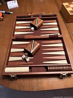 Open backgammon case showing game board, checkers, dice cups, and dice inside.