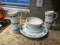 Complete set of 4 mugs and plates displayed with holly leaf festive pattern on countertop.
