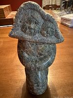 Front view of the Inuit soapstone sculpture showing the mother holding her baby with detailed facial features on a hooded coat.