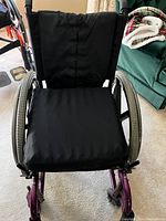 Front view of the InvaCare wheelchair showing black seat, backrest and purple steel frame, missing armrests