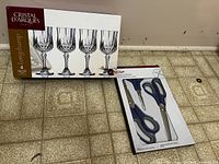 Box of 4 Longchamp Cristal d'Arques wine glasses and pack of 3 Chef scissors side-by-side on tiled floor.