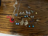 Photo showing assorted costume jewelry spread on wooden surface, including several pairs of earrings and two necklaces.