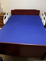 Front view of the queen size medical bed showing wooden footboard, blue mattress, and white side rails.