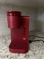 Front view of red Keurig coffee machine showing brand on coffee pod holder and control buttons on the side panel.