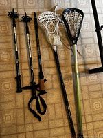 Photo showing the two lacrosse sticks and three walking sticks on floor tile background.
