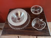 Photo showing a vintage Candlewick by Imperial Glass condiment bowl with matching under plate, a glass apple-shaped bowl with leaf detail, and three clear glass bowls with beaded rims.