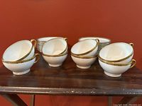Four stacks of white porcelain heart-shaped teacups with gold rims and handles shown on a wooden surface.