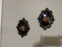 Two vintage oval convex framed dried flower bouquets hanging on a wall, showcasing size comparison and style.