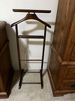 Full view of the wooden pant and shirt hanger stand between two dressers, showing its height and construction details.