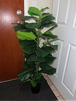 Artificial fiddle leaf fig tree with large deep green leaves in a black pot placed near a door indoors.