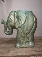Side view of the ceramic elephant plant stand showing textured green and gray finish and foliage detail on one side.