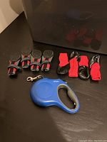Photo showing two sets of dog footwear and one blue retractable leash on black surface.