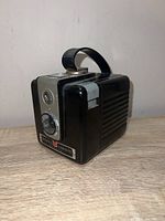 Side-angle photo of Kodak Brownie Hawkeye camera showing black ridged body, silver front panel with twin lenses, and black handle on top.